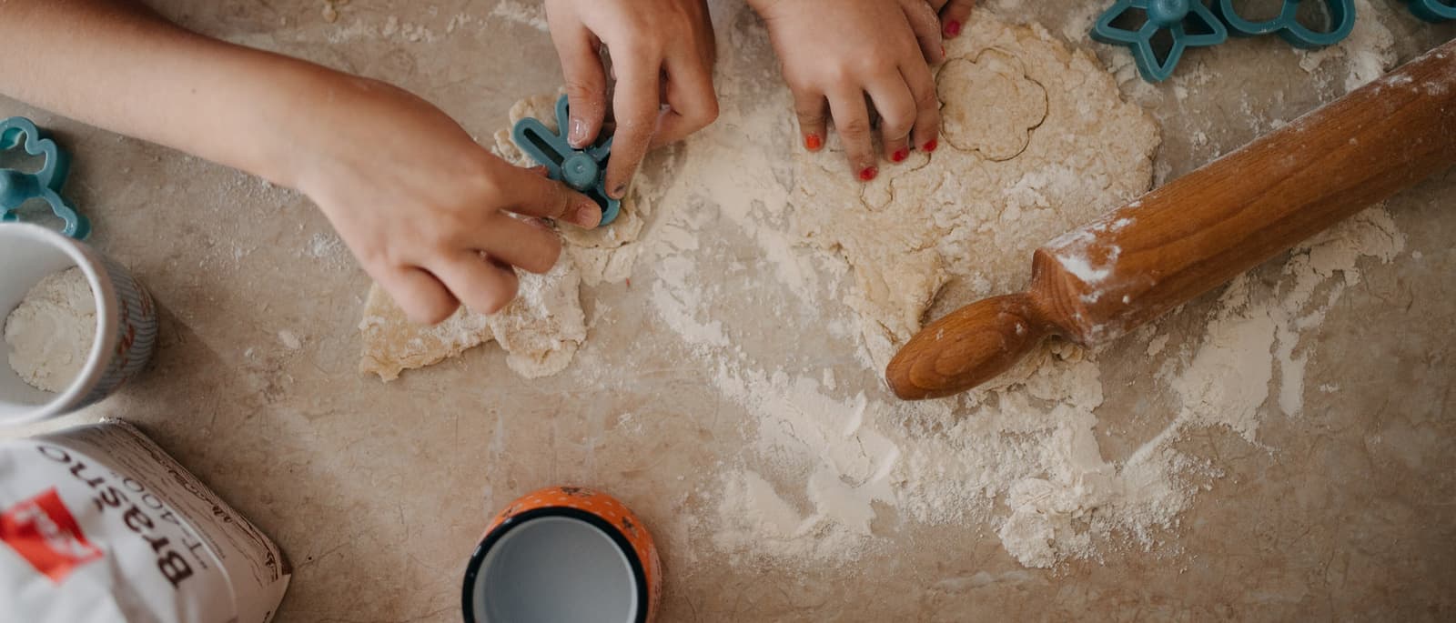 Hands pressing cutters into rolled dough on a flour-dusted kitchen counter